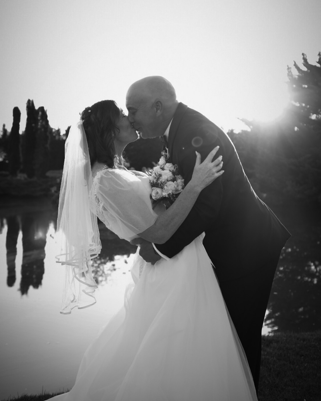 Bride and groom kissing beside a lake at sunset, black and white