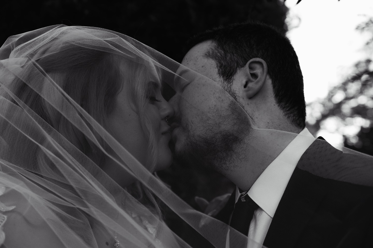 Couple kissing beneath a veil in soft evening light, black and white