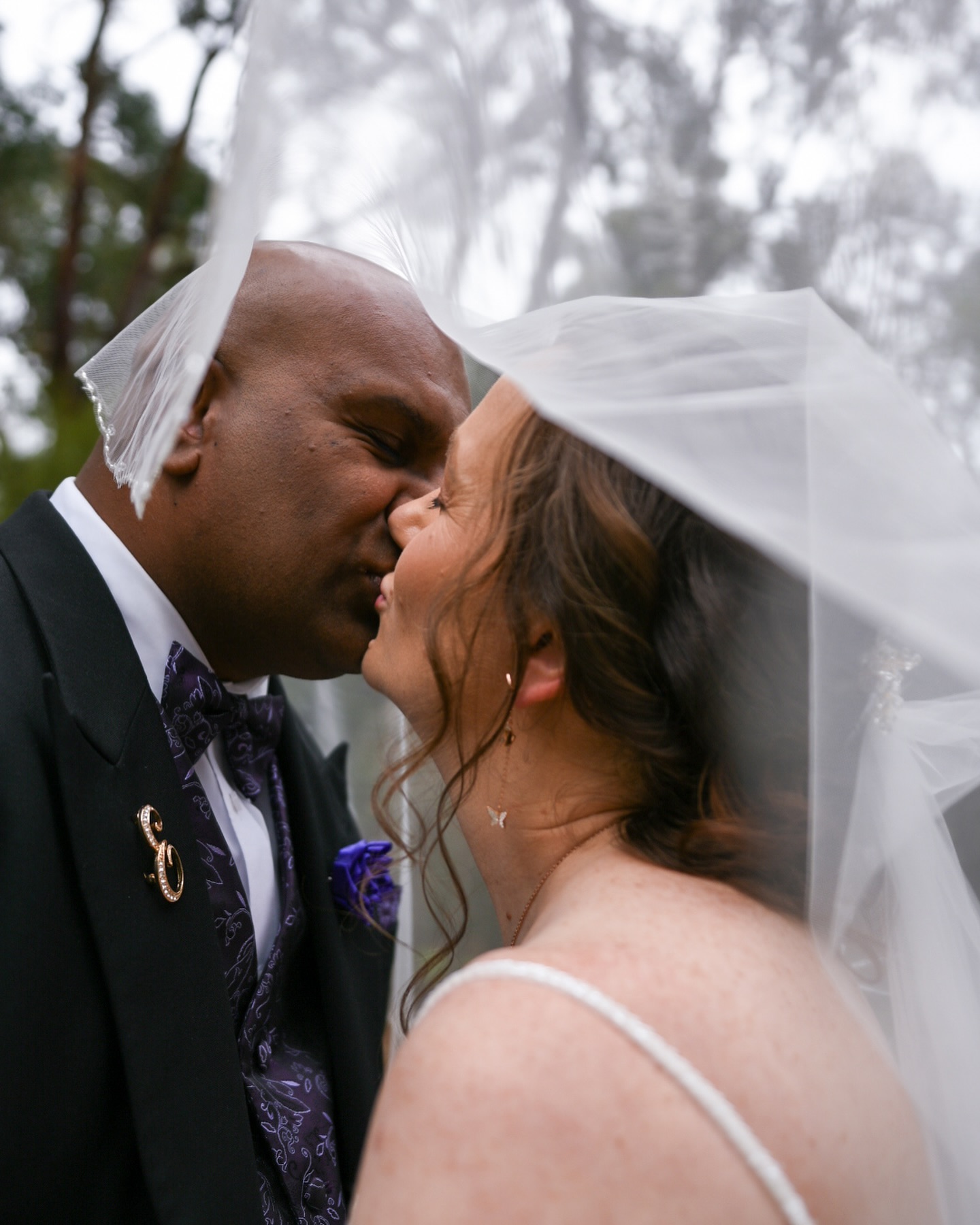 Couple kissing under a veil among tall trees